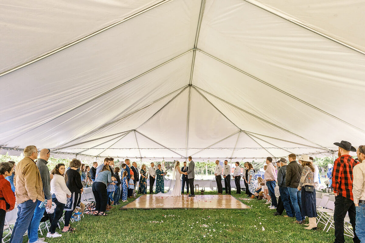 A bride and groom stand under a tent at their outdoor Veneta farm wedding.