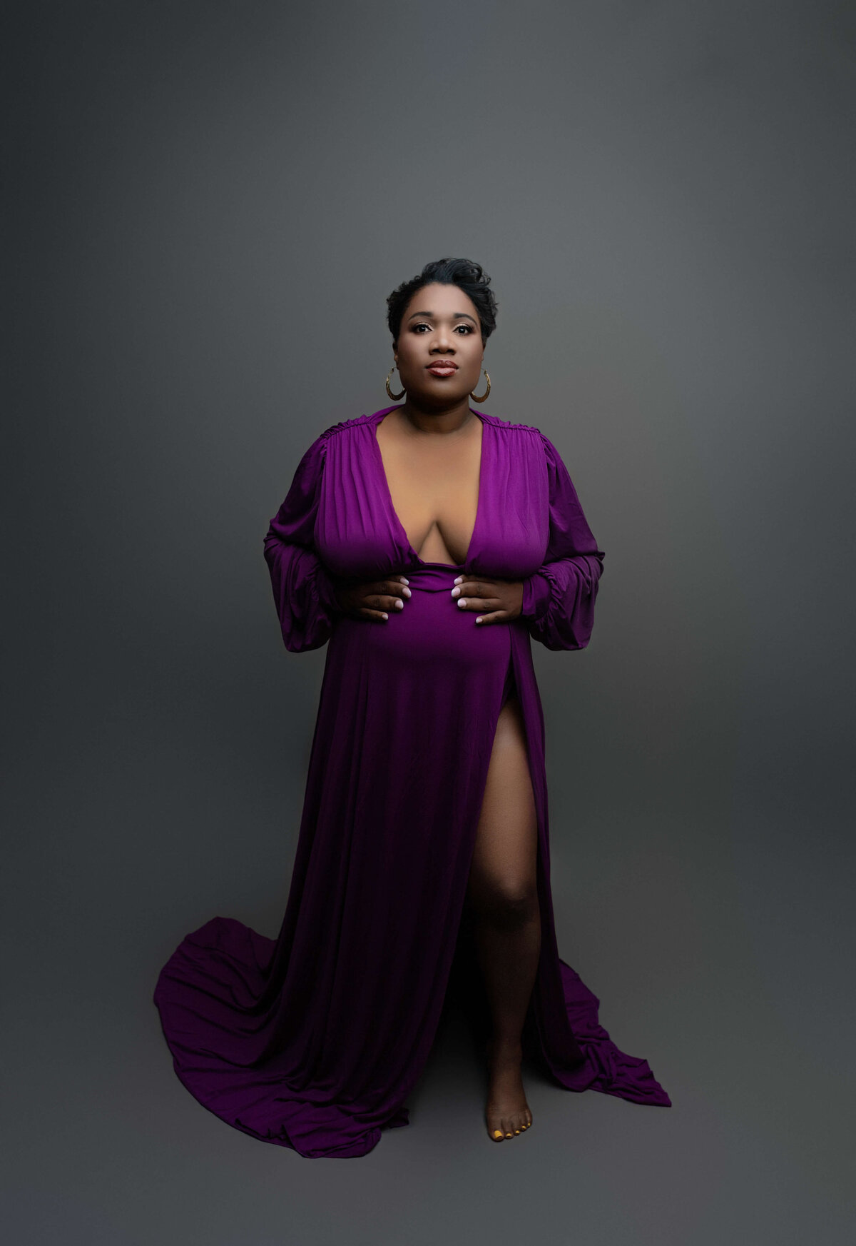 A powerful pregnant black woman stands in a purple dress in a studio