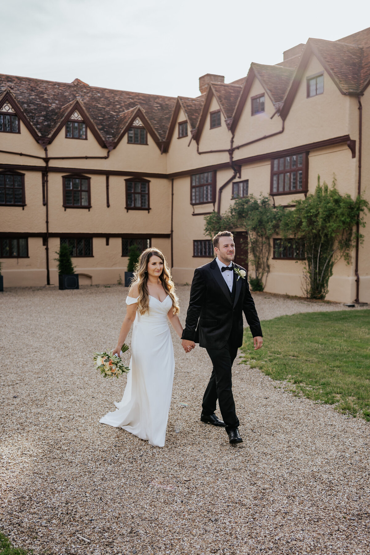 Bride and groom walk holding hands, walking away from the tudor house at Ufton Court at golden hour