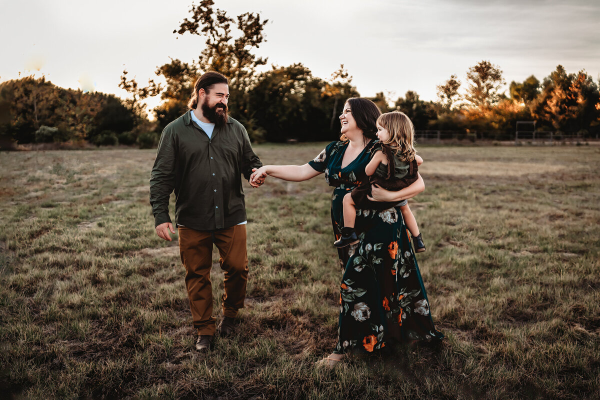 Parents holding hands and walking together in a field at sunset, photographed by San Diego family photographer.