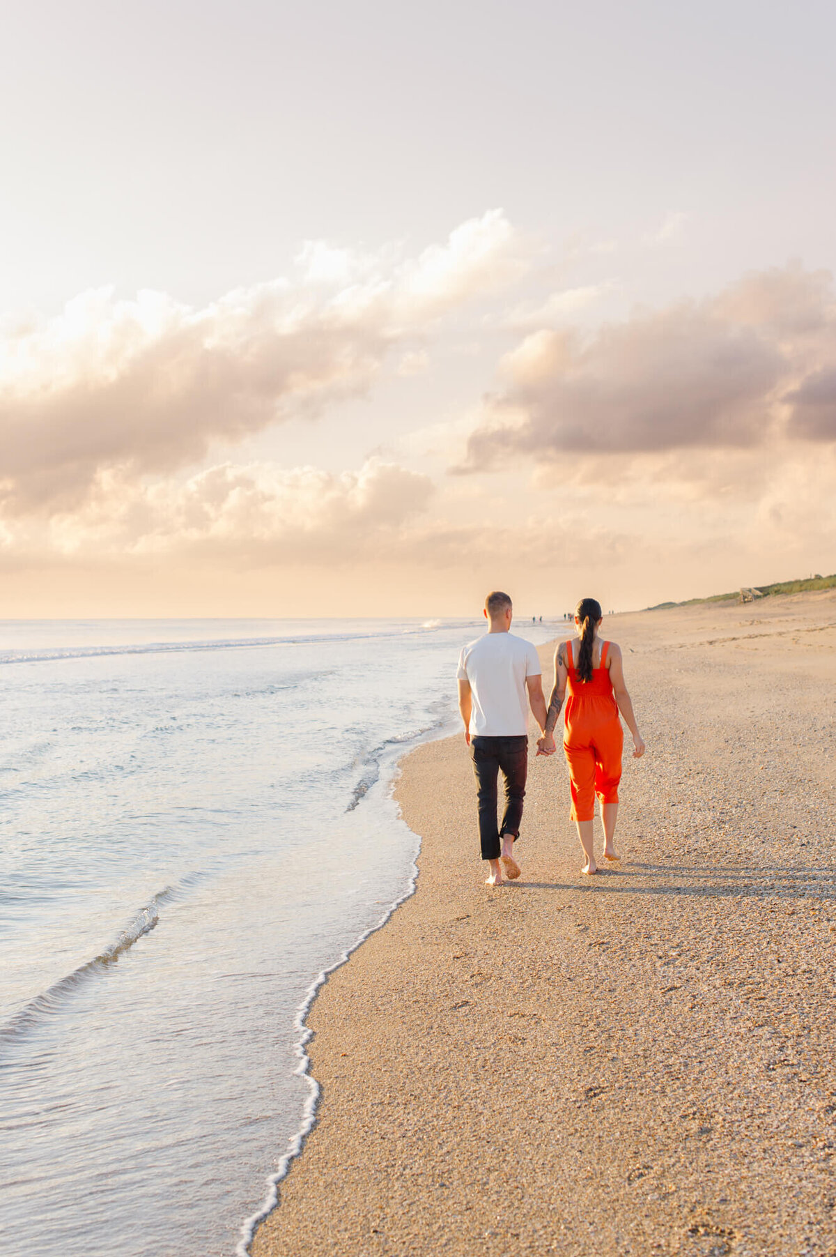 Couple walking away down the beach next to the shoreline at sunrise