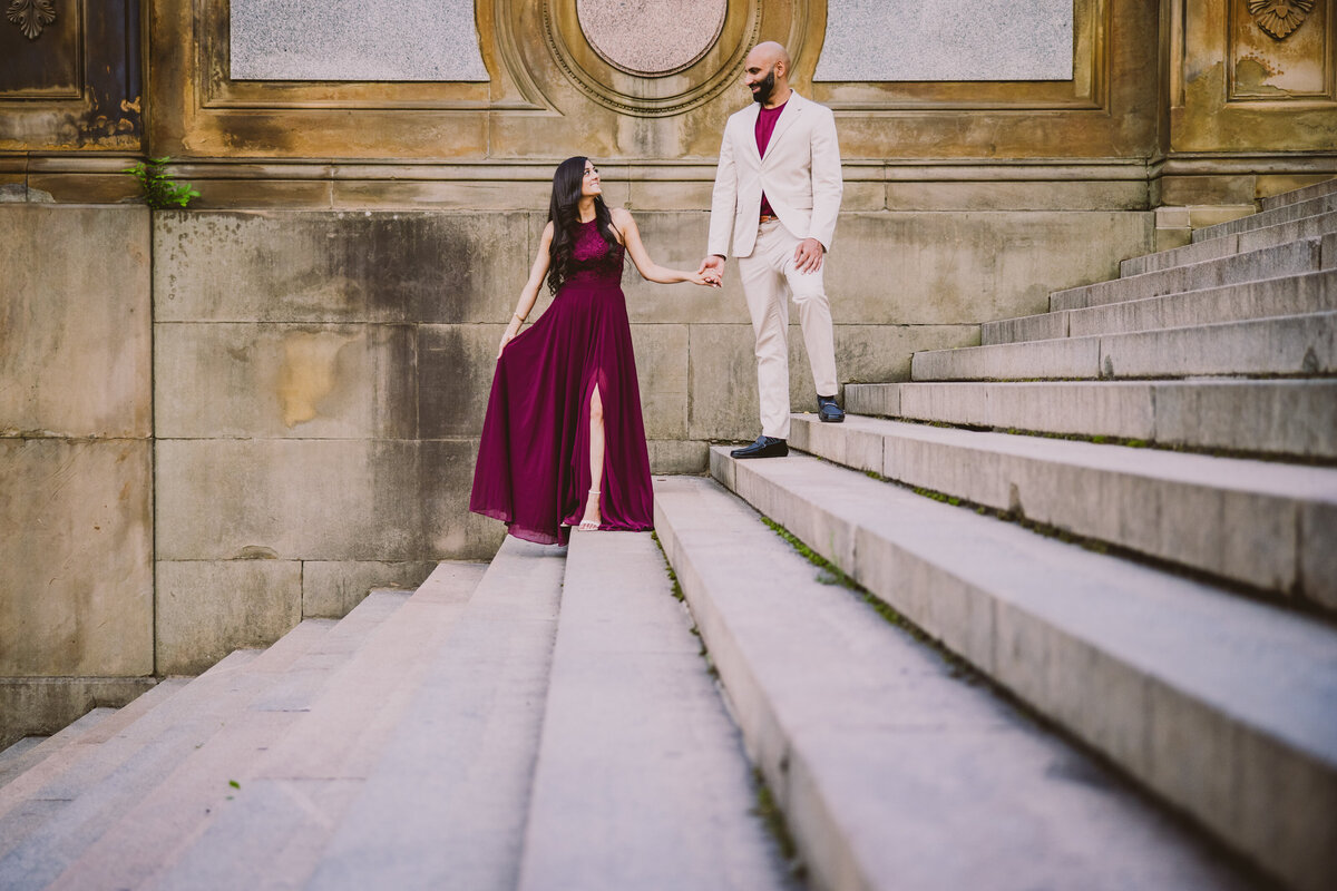 A couple in red outfit during their engagement session on some steps at bethesda terrace at central park