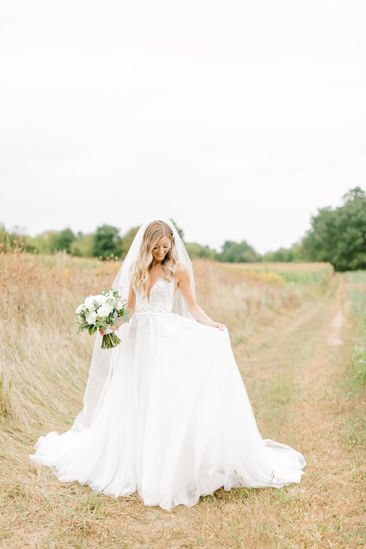 bride in a field fluffing dress and smiling