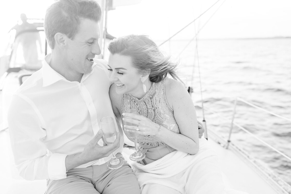 Engagement photo of couple laughing on a sailboat with champagne