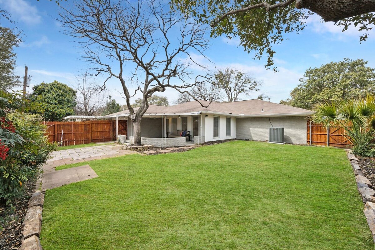 Spacious fenced backyard at 3120 Chapel Downs Dr Dallas TX with mature trees, manicured lawn, and partial patio view — Haven Realty Group.