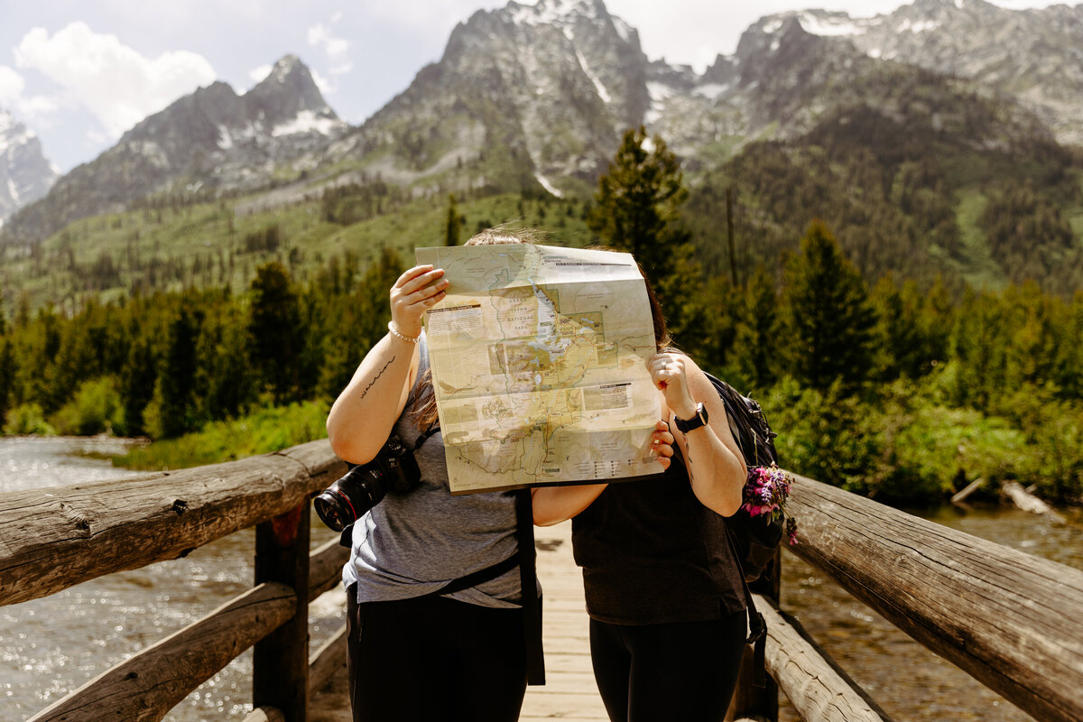 Couple sharing a kiss hidden behind a map with the grand tetons behind them