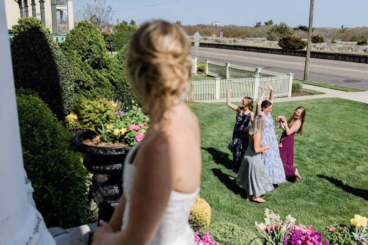 Bride looking back at 4 women laughing after the bouquet toss in the front lawn of the Peter Shields