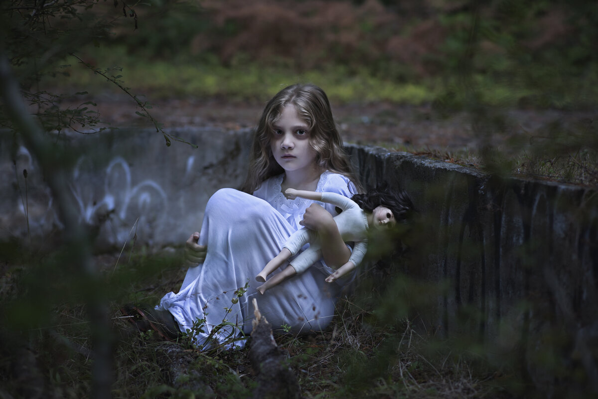 Ghost girl sitting with her doll in an  abandoned house foundation