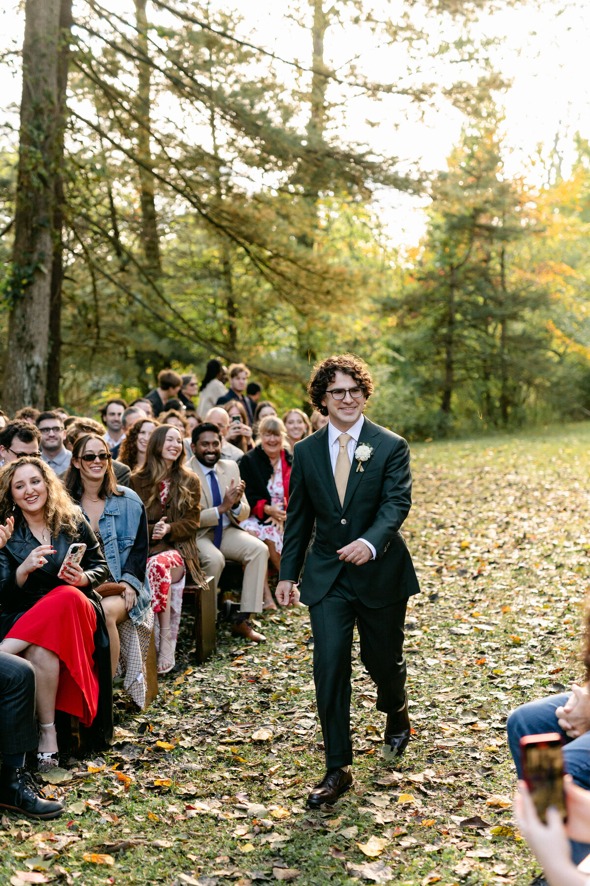 Groom walking down the aisle with guests smiling in back