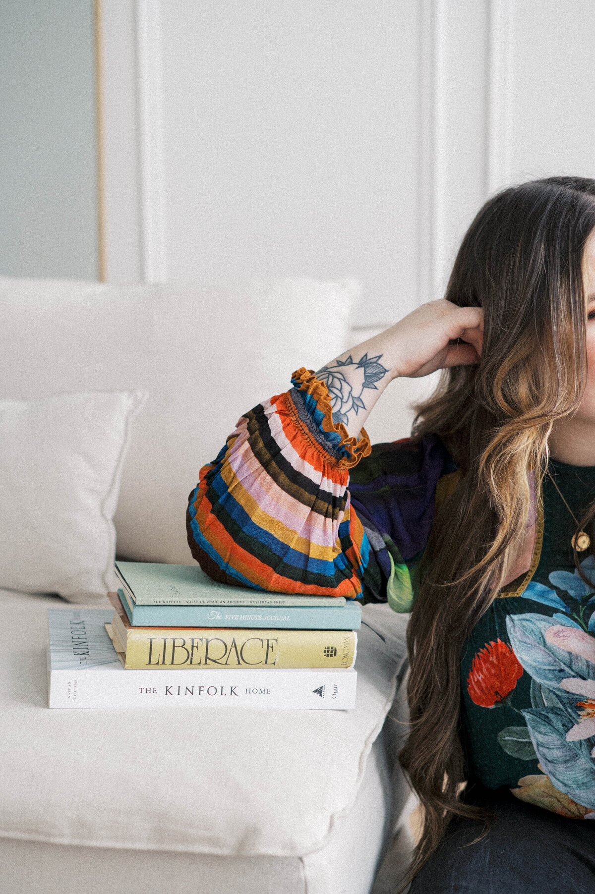 Woman with long hair in colourful shirt leaning on stack of books on a couch