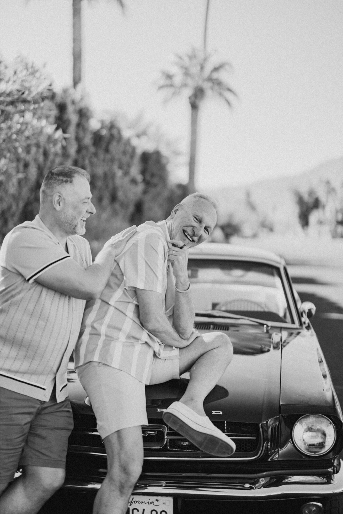 Black and white image of couple sharing a sweet kiss in a convertible, framed by vintage style and Palm Springs romance.