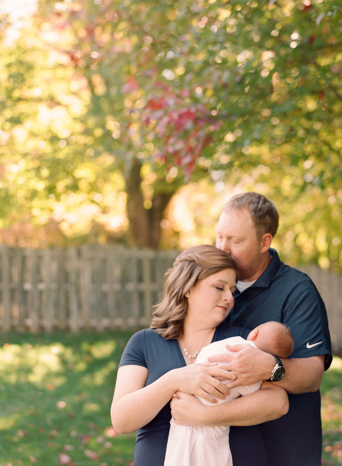 New parents snuggle outside under a fall tree in Greensboro NC. Image by Raleigh newborn photographer A.J. Dunlap Photography.