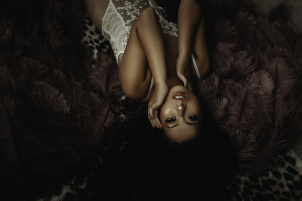 Boudoir Photographer, a woman lays on the ground with purple feathered wings beneath her