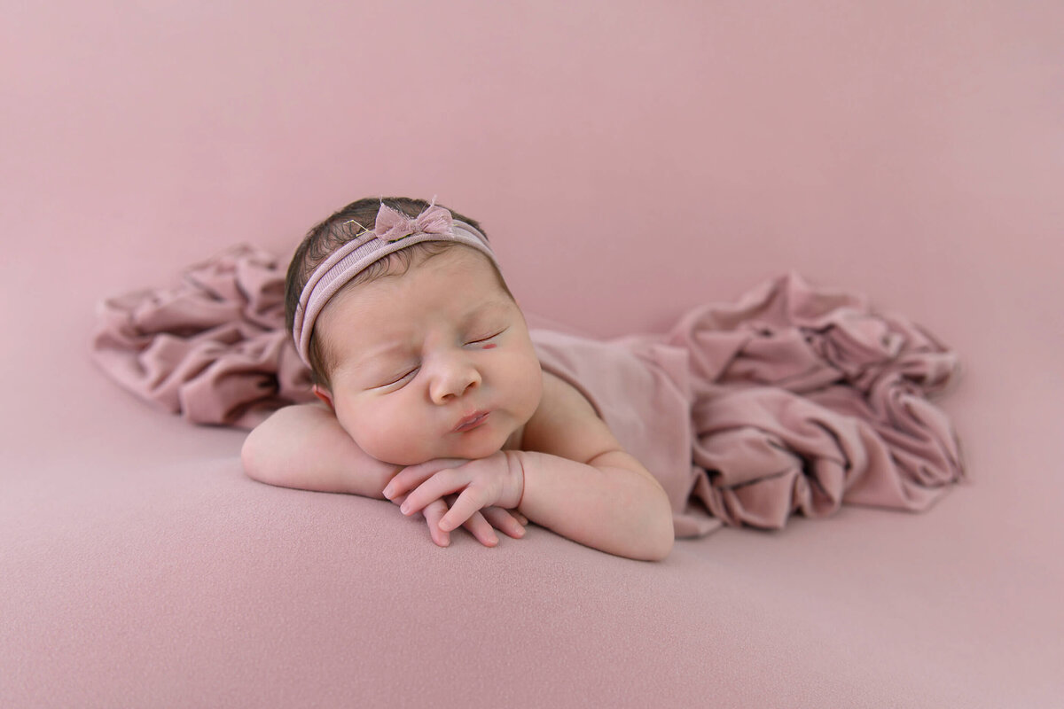 newborn girl laying on a pink background for her newborn photos in Burlington, ON