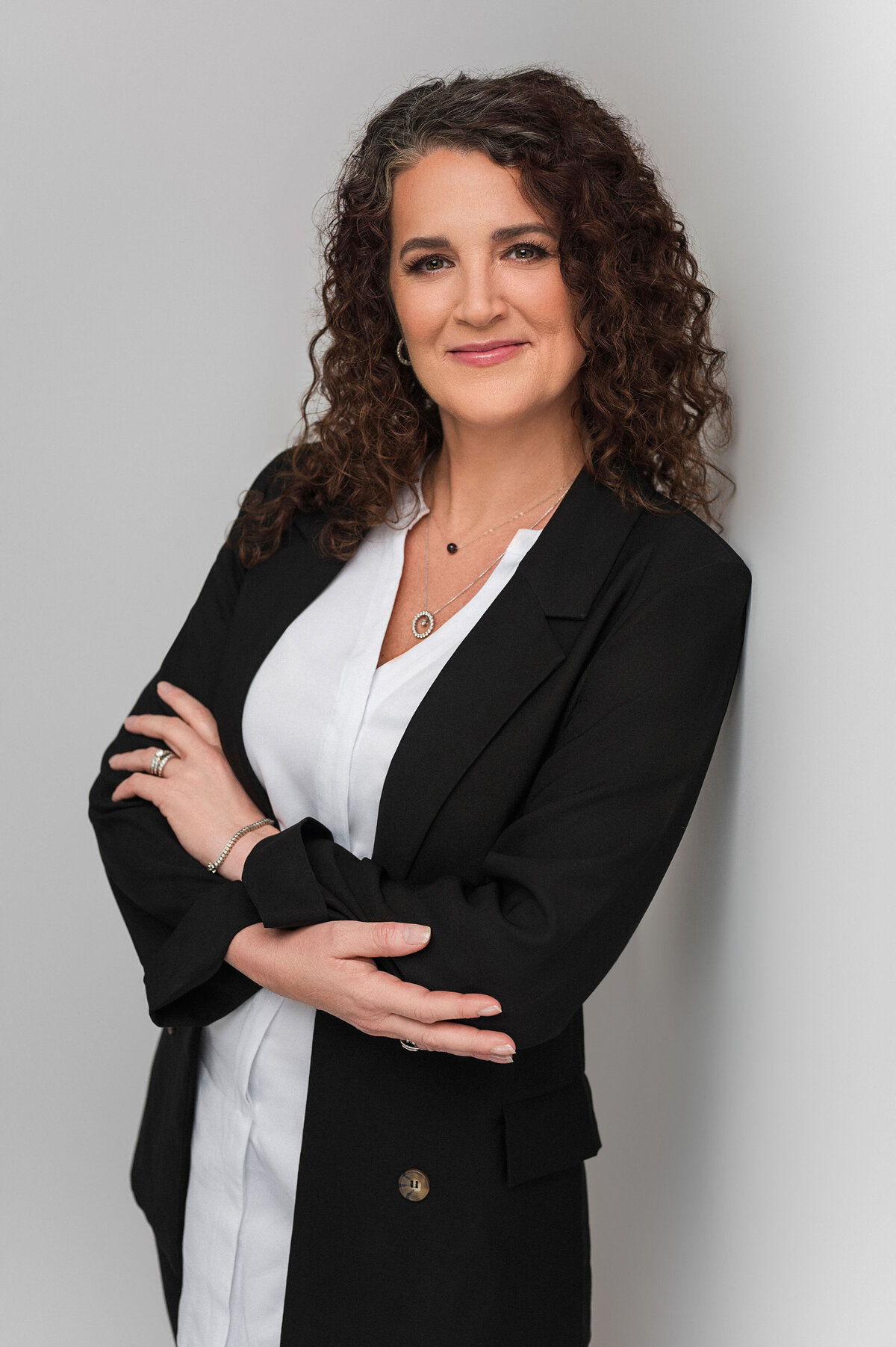 Confident woman in a black blazer, crossing her arms and smiling
