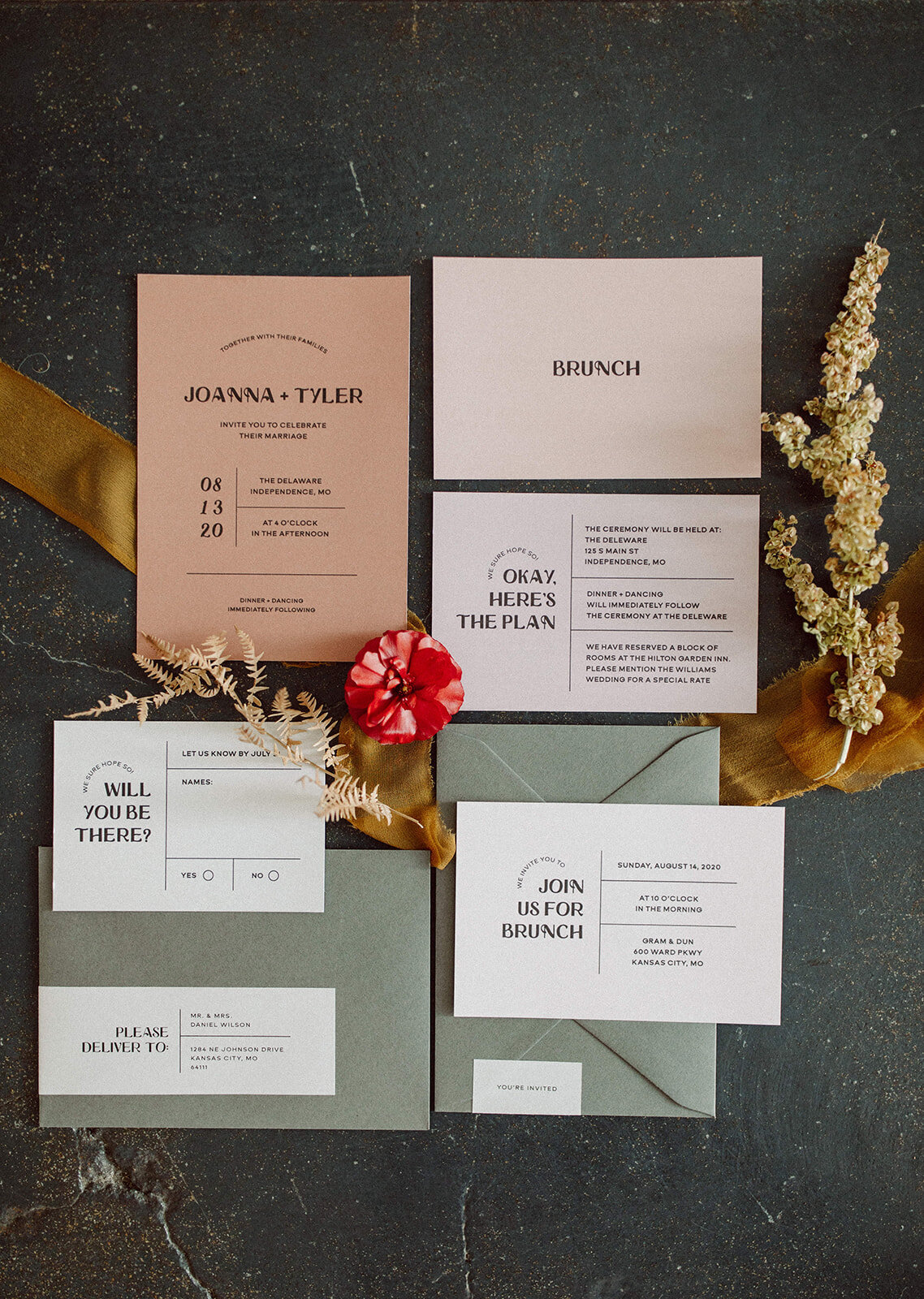 Mixed off-white, peach and mauve-colored wedding stationery with black font atop ribbon on concrete with stems flower.