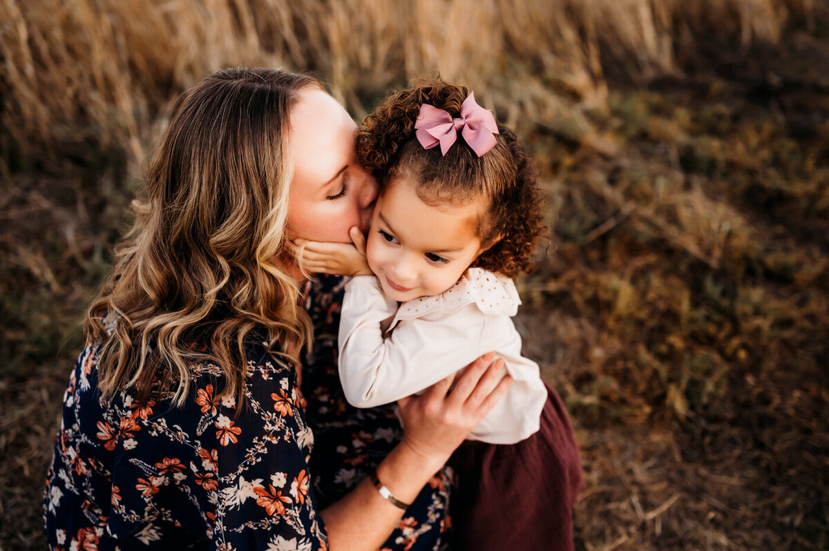 Mama kissing baby girl while baby girl holds mamas face