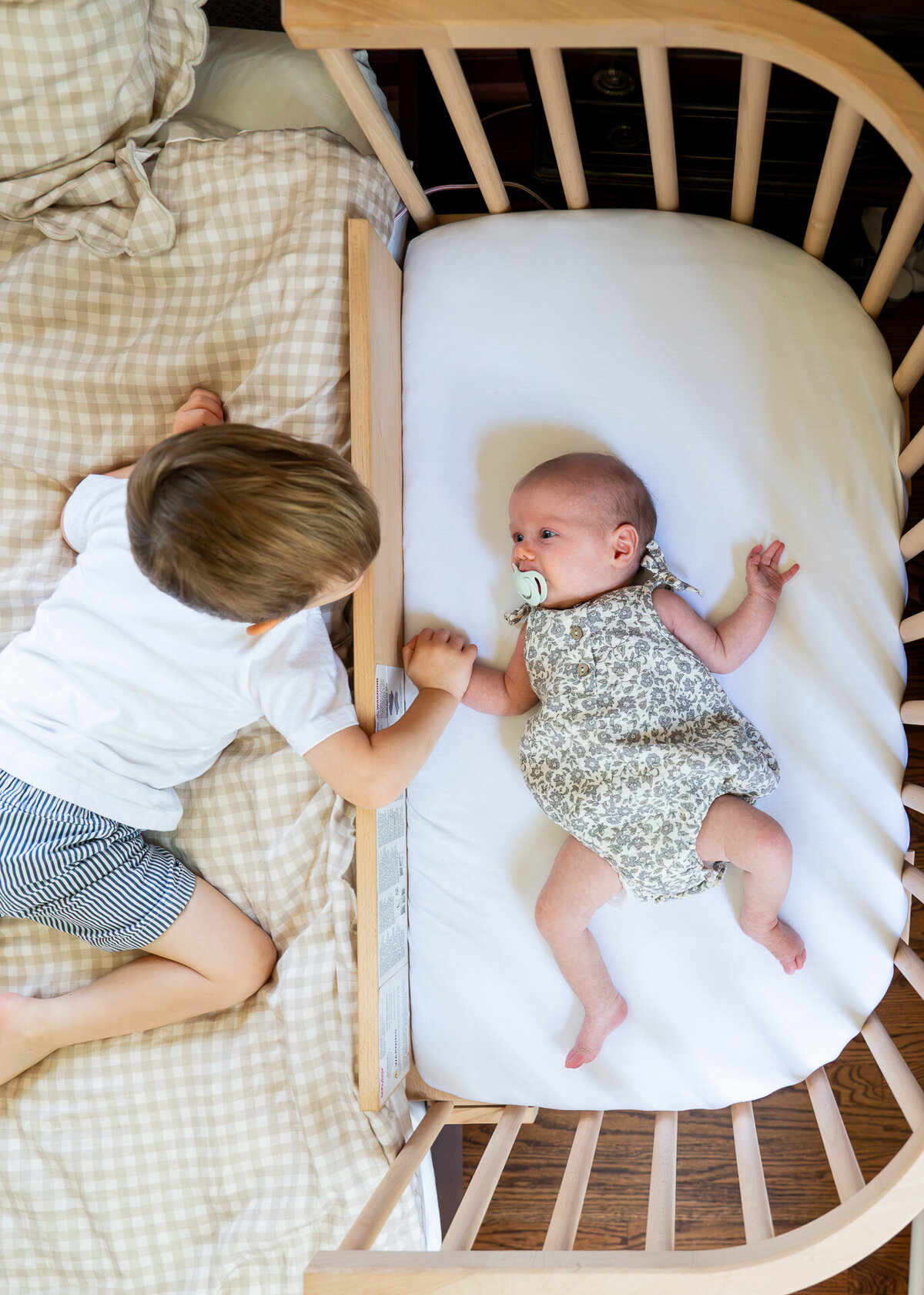 toddler brother reaching into cosleeper toward newborn sister with pacifier