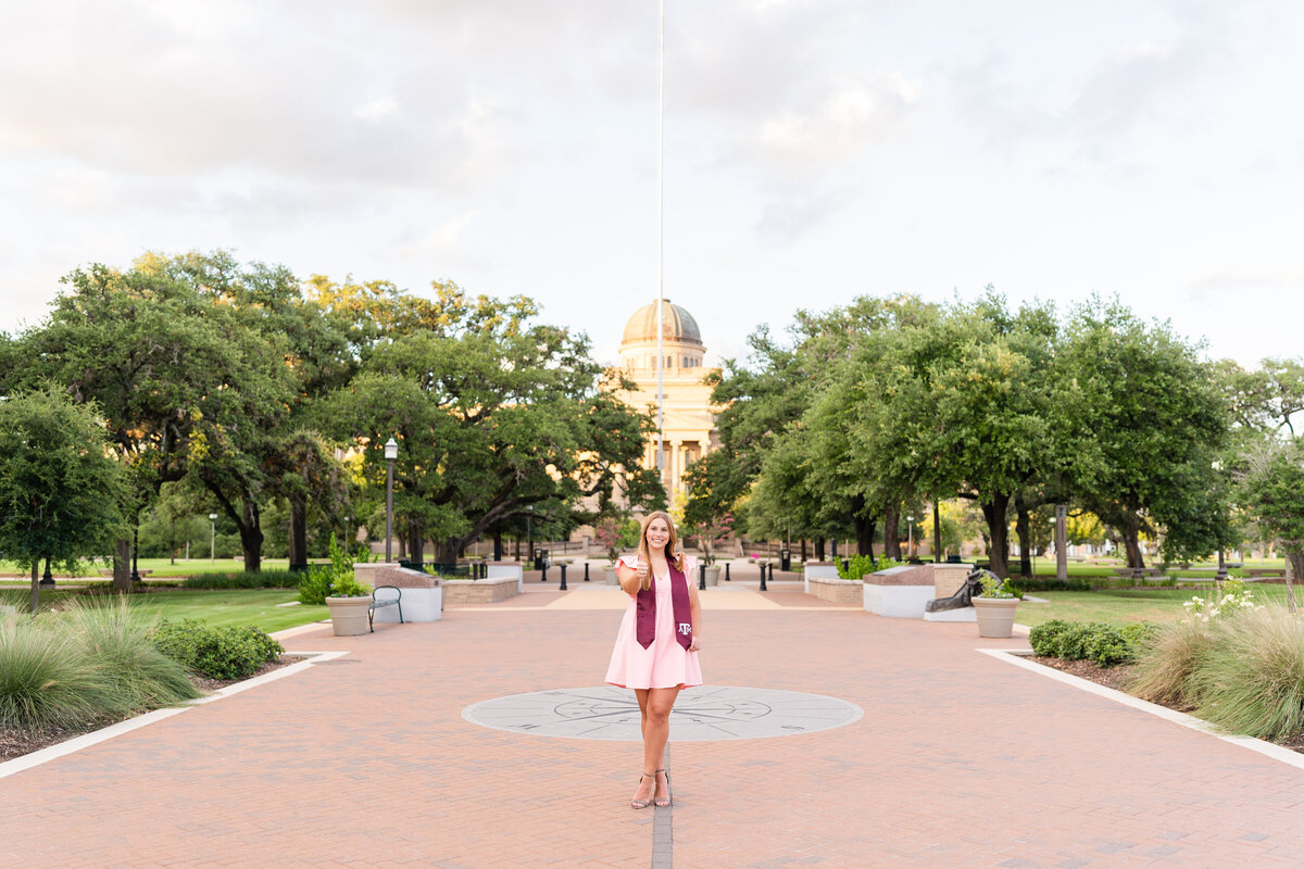 Texas A&M senior girl showing a gig em in front of the Academic Building in Military Plaza at sunset