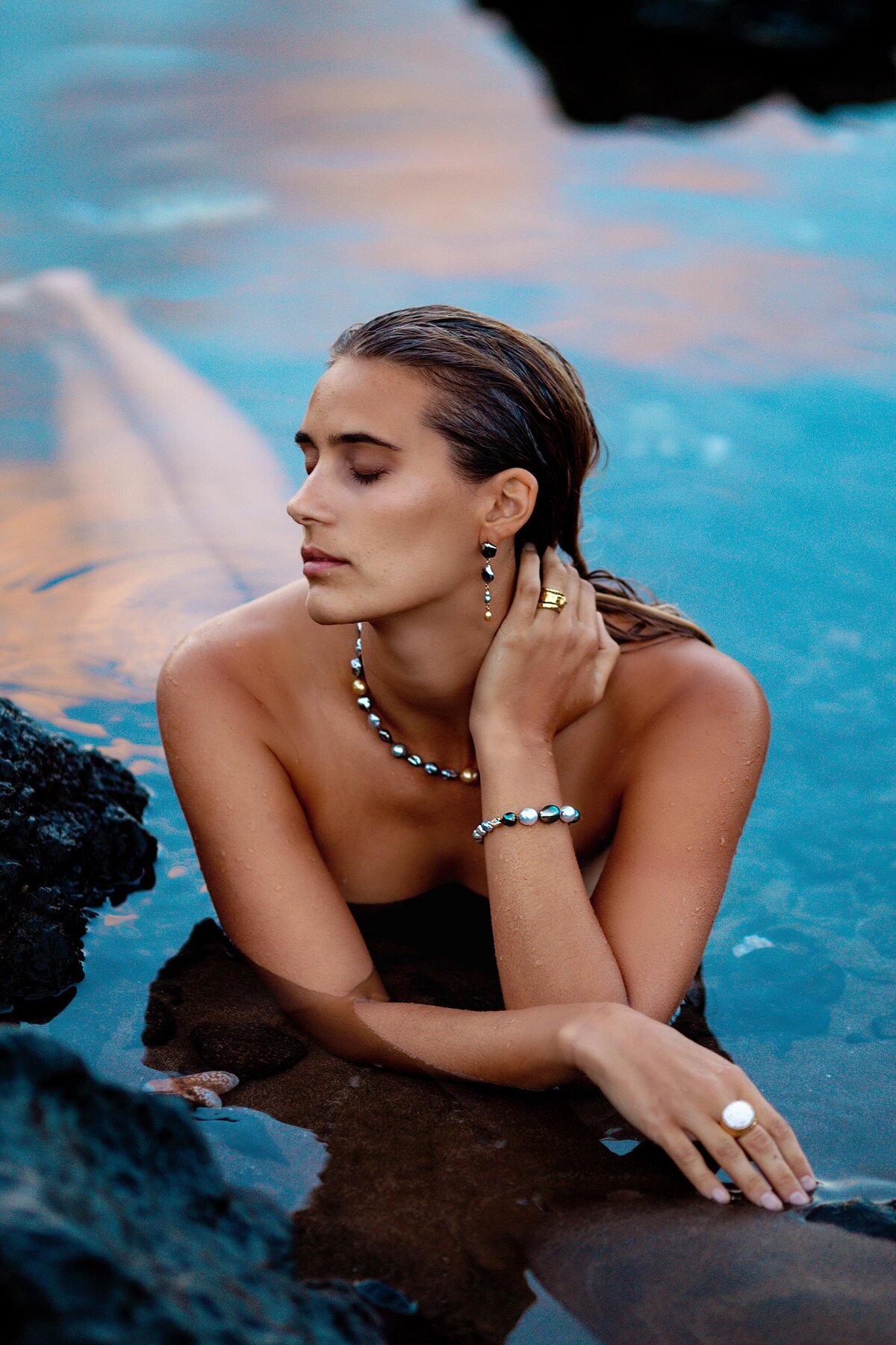 Stunning woman poses in shallow water with her eyes closed during her boudoir portrait session in Hawaii