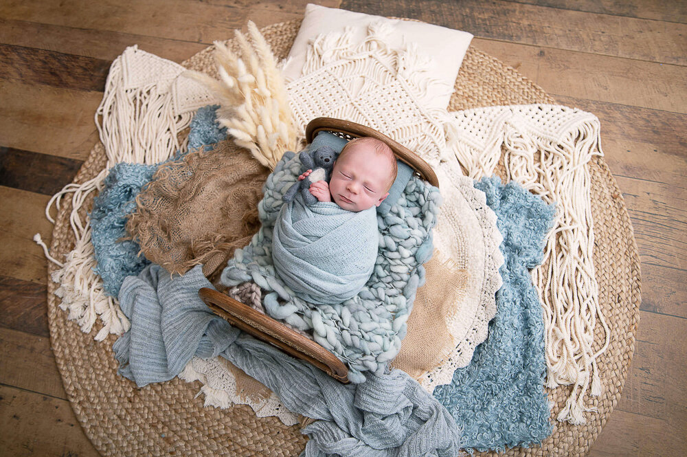baby boy wrapped in blue in a tiny bed with blue and cream colours for his baby photography session.
