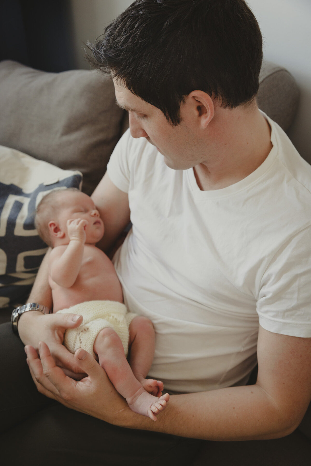 Livsstilsfoto  av far som holder babyen sin i armene sine, fotografert på skrå ovenfra og ned. Far ser på babyen sin.