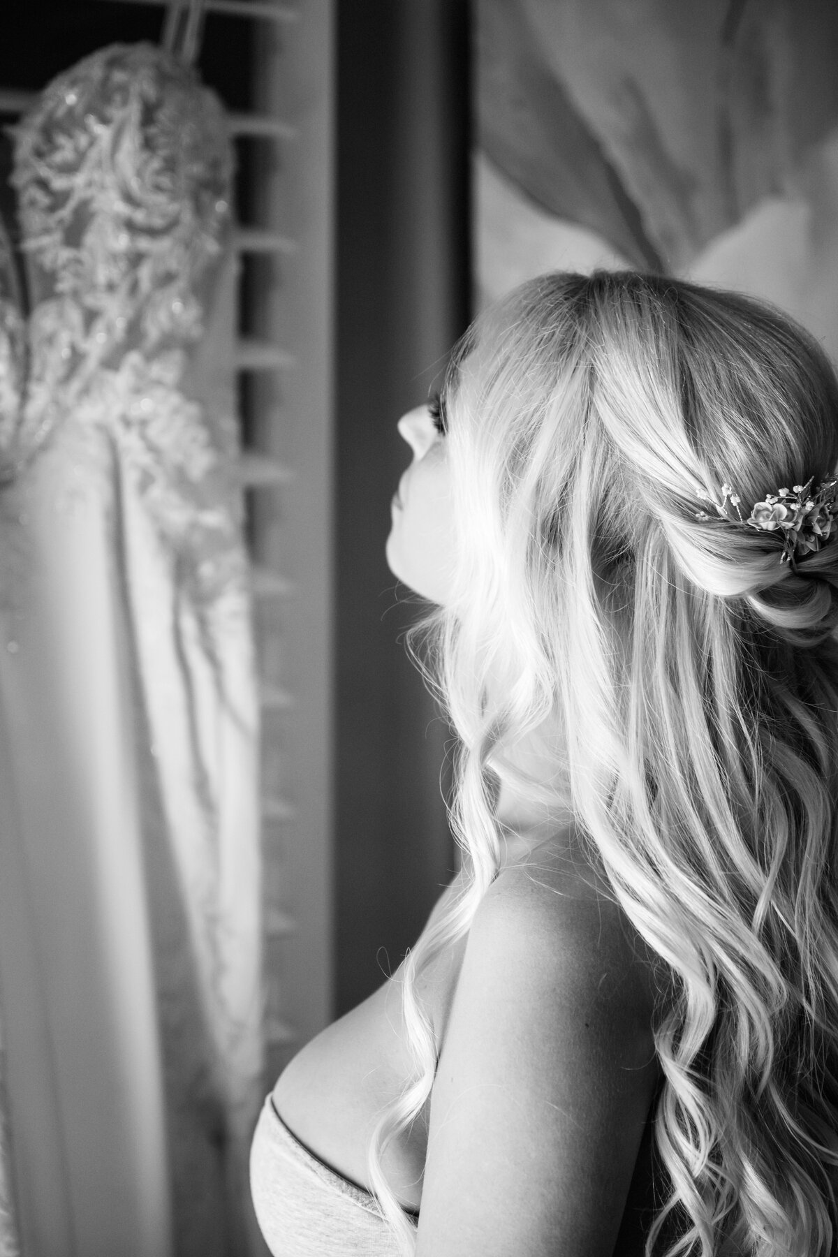 Black and white picture of a bride looking at her hanging wedding dress