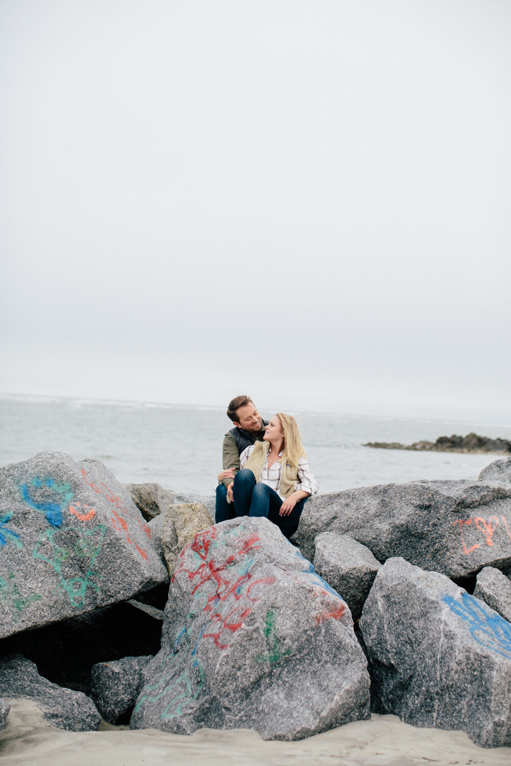 Engaged couple sitting on rocks at Folly Beach during their Charleston engagement photos.
