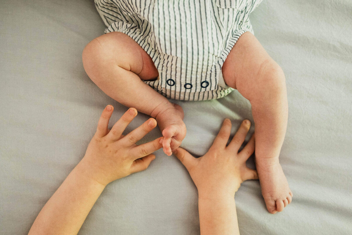 A tender close-up of a newborn's tiny feet held by their older sibling, highlighting family connections.