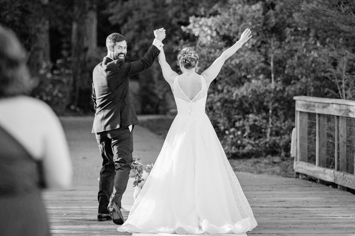 Bride and groom walking down the aisle, celebrating their new journey together in a joyful black-and-white moment, filled with laughter and cheers.