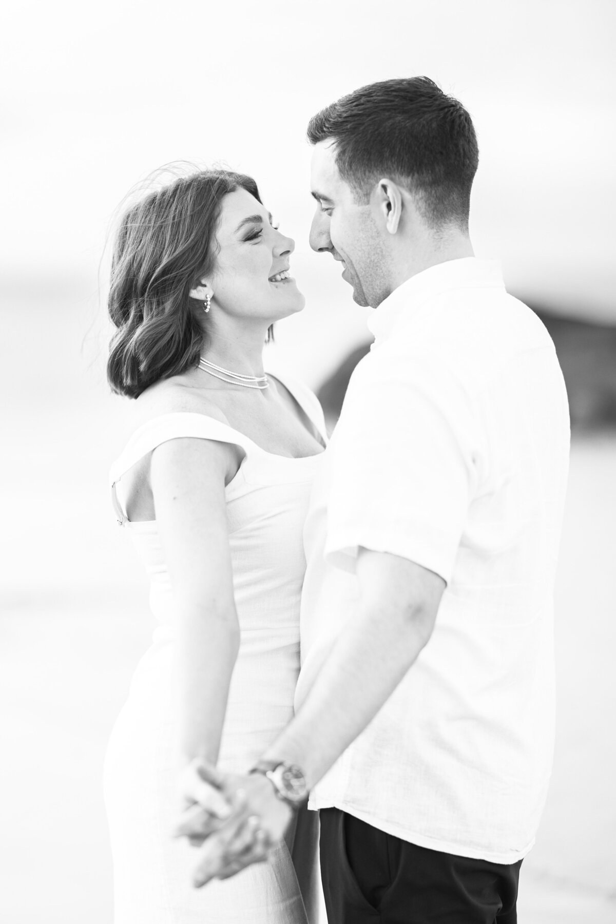 A black and white image of a couple holding hands and dancing on Wingaersheek Beach during their engagement session.