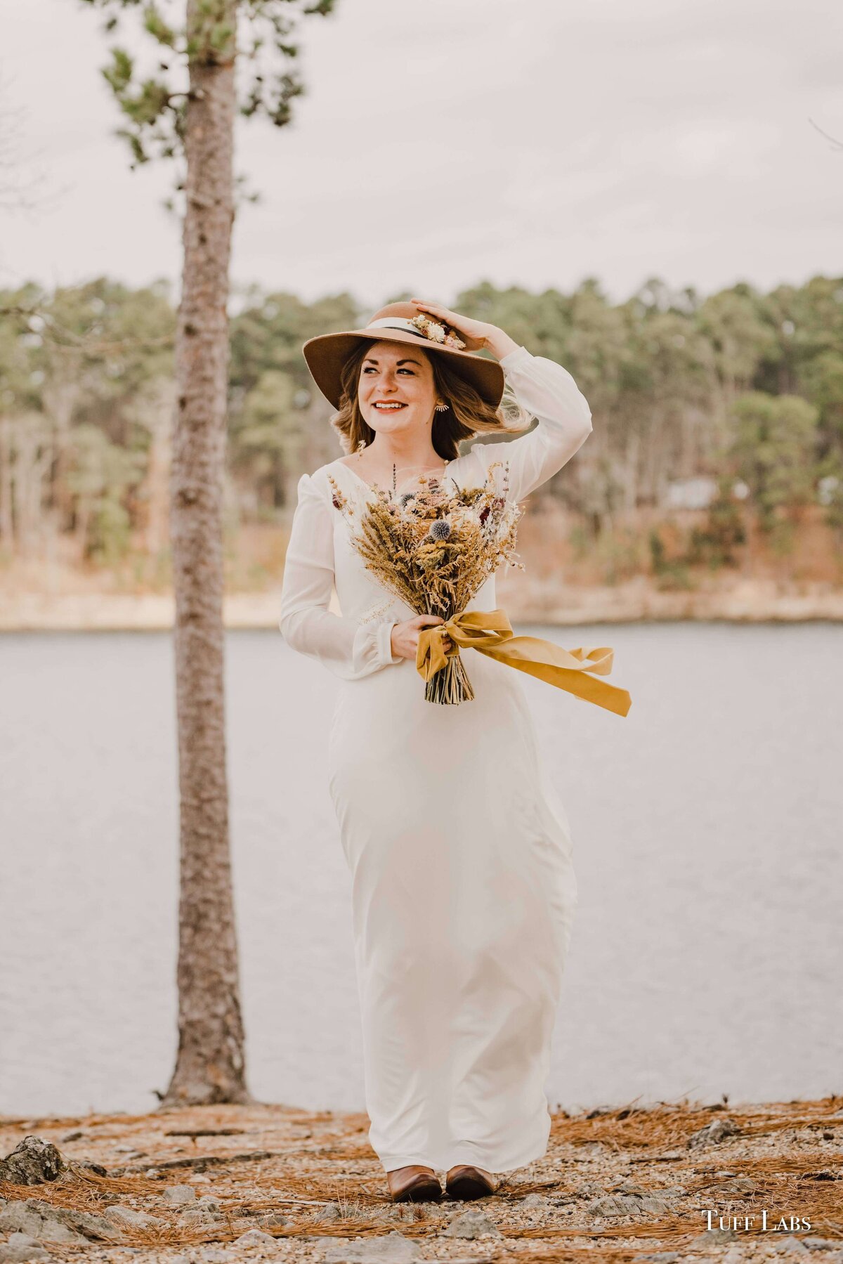 A bride holds her hat and dried flower bouquet.