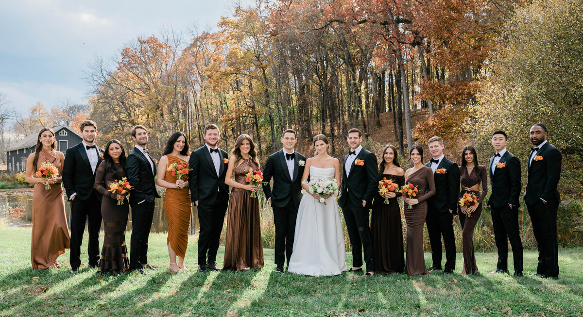 the bride, groom, and their wedding party, surrounded by tall trees with golden leaves.