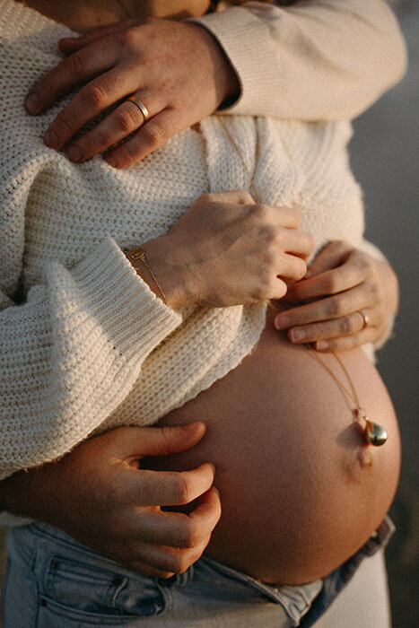 Homme entourant de ses bras sa femme enceinte au ventre rond apparent. Séance photo  grossesse par Kamescop.