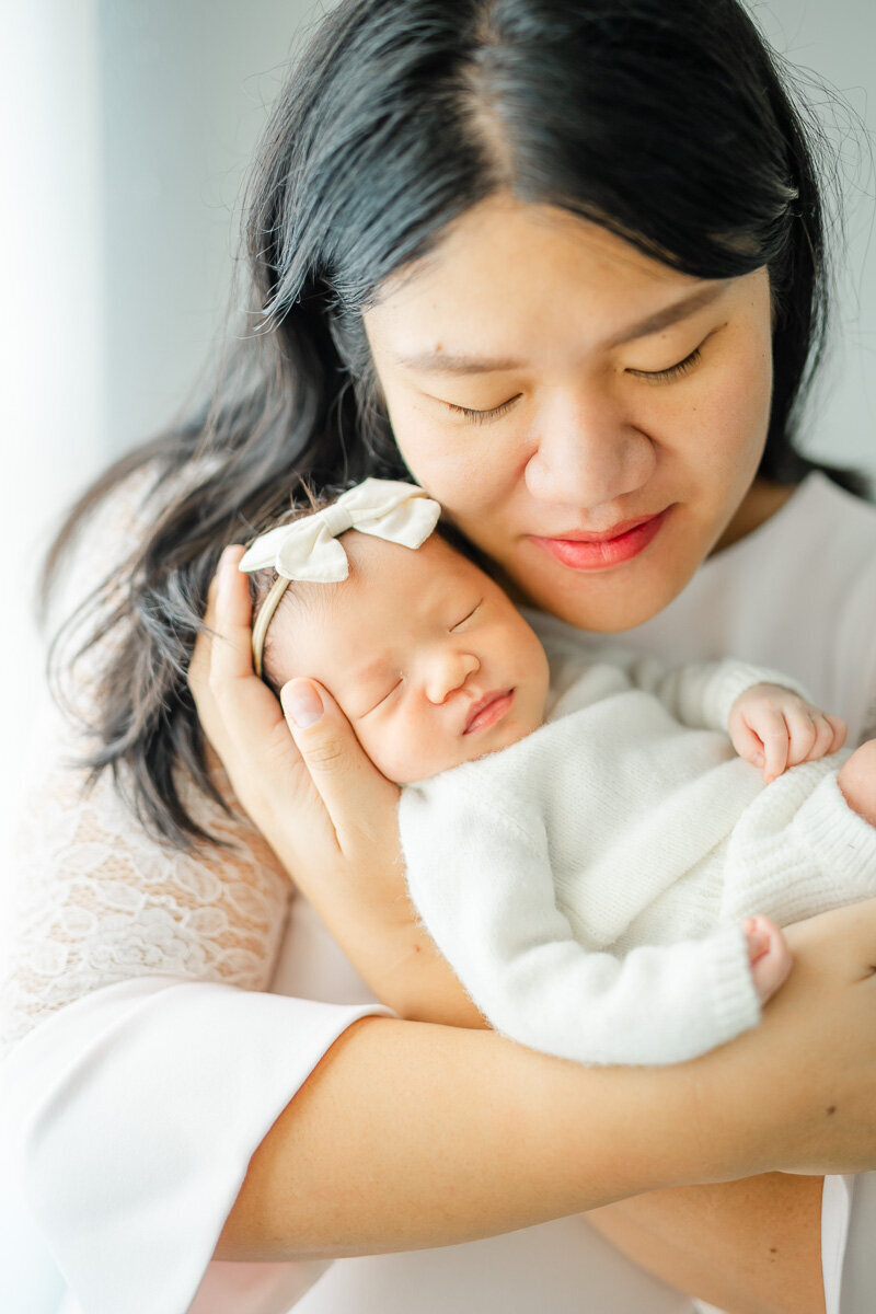 a mom poses with her newborn baby girl and lays her cheek against her infant's head, beautifully captured for their infant portraits in Austin, TX.