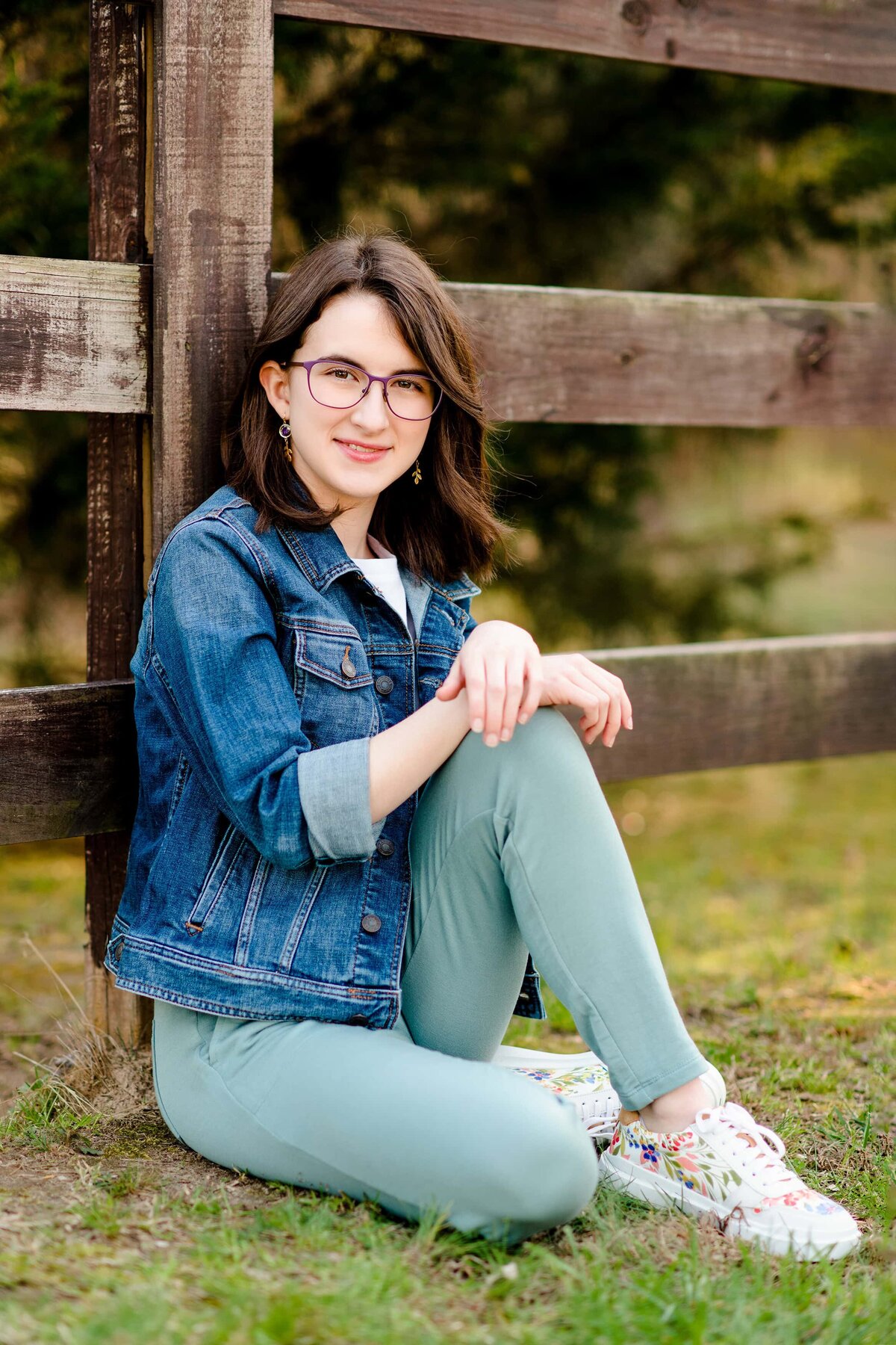high school senior from cata sits against a fence wearing green pants and a jean jacket