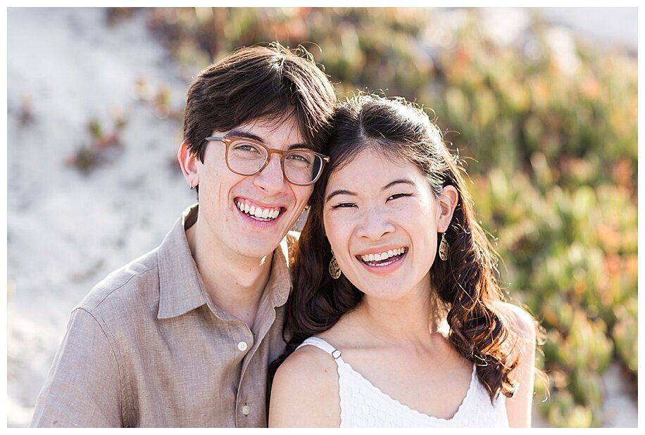couple sitting in sand dunes smiling