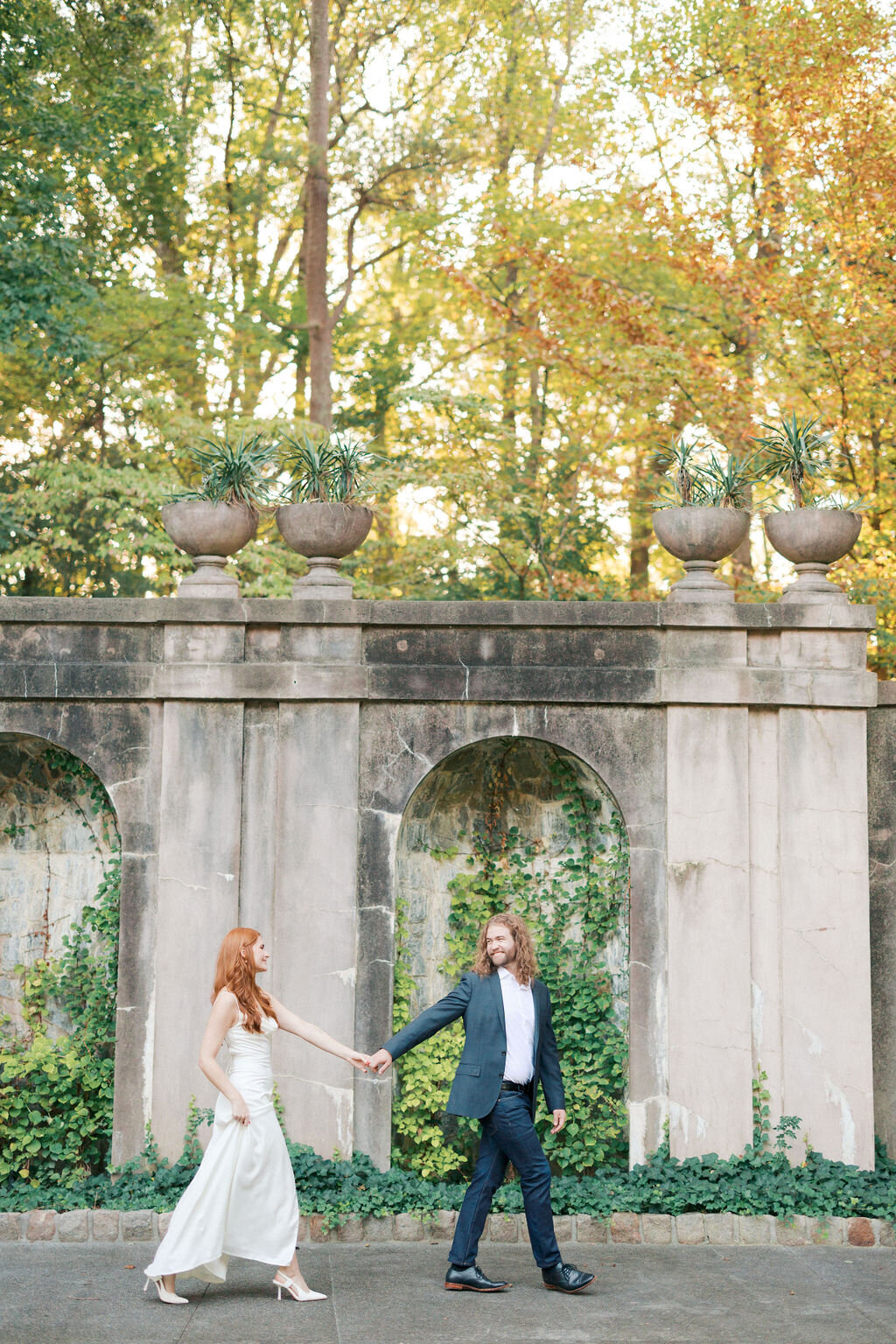 Man holds hands with woman in white dress with stone archways at Atlanta History Center