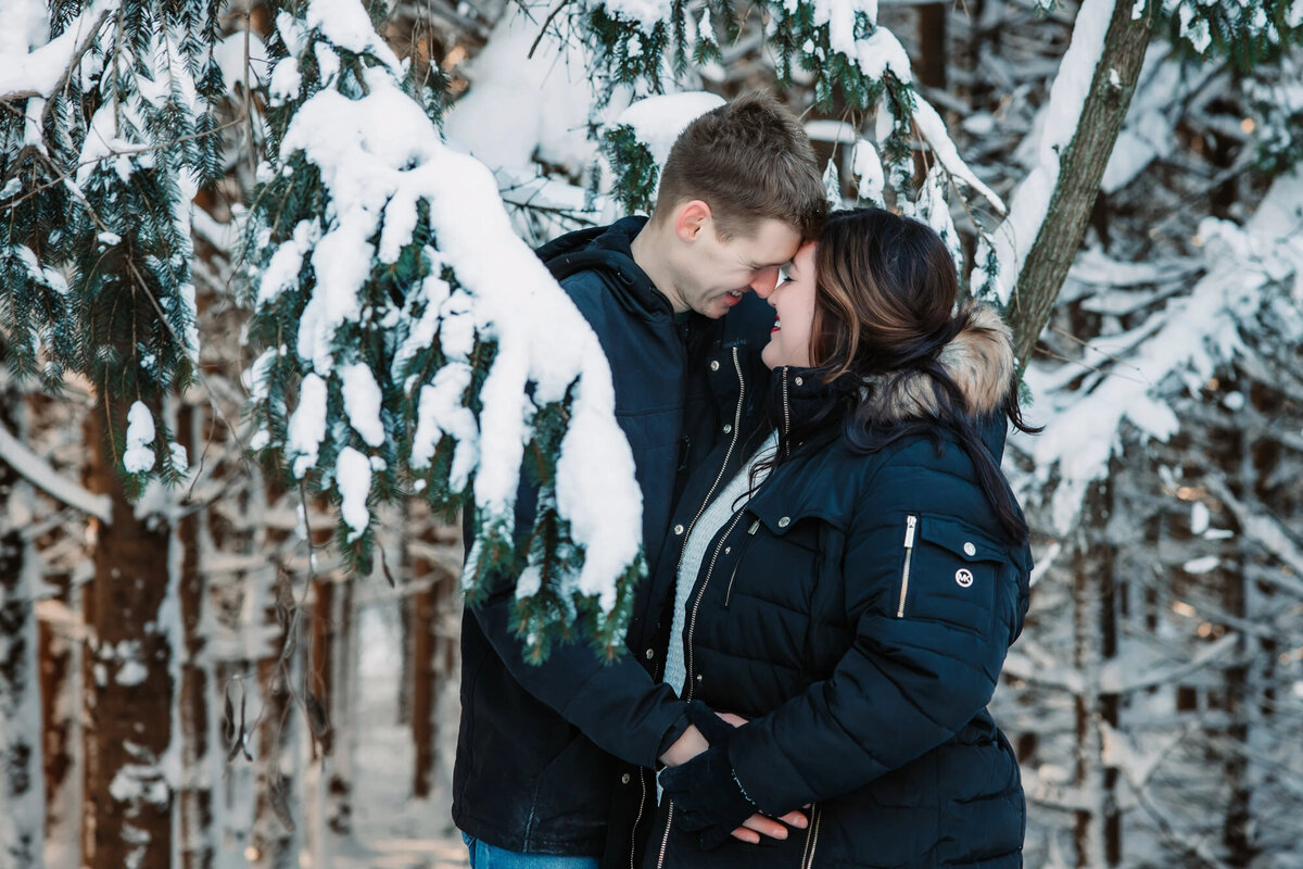 man and woman are head to head in a snowy forest while wearing coats