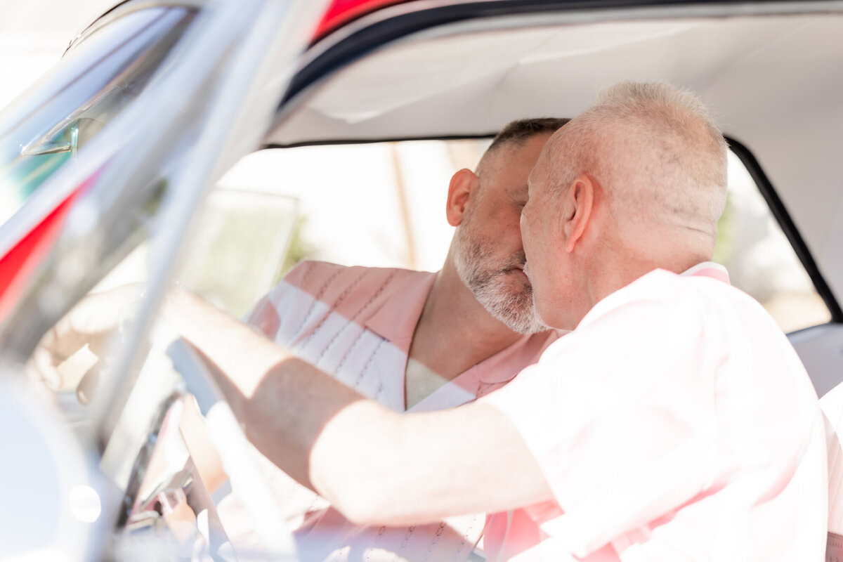 Close-up of couple inside vintage car, sharing a joyful moment through the window with soft morning light.