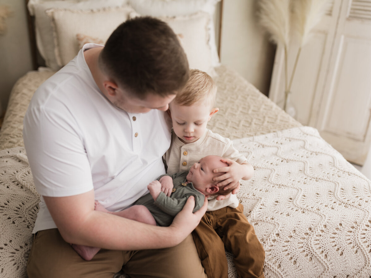 dad and son holding newborn baby boy in green onesie
