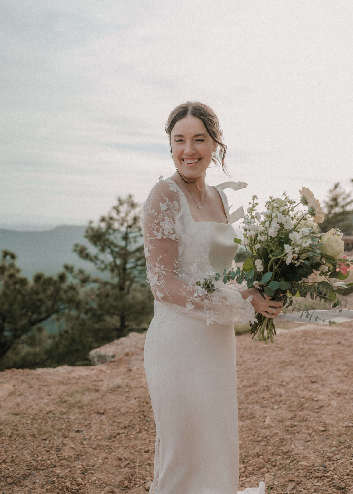 Bride holding bouquet and smiling on side of Mogollon Rim in Payson, Arizona