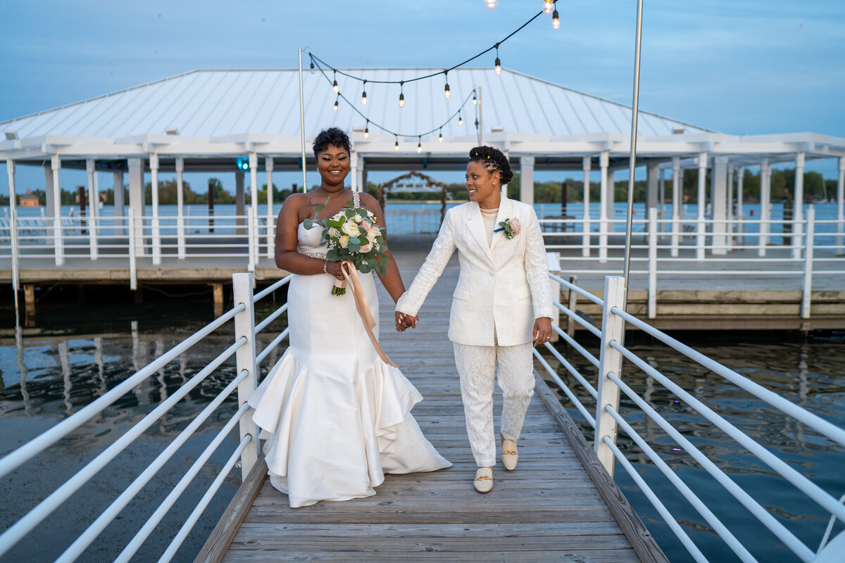 Brides holding hands walking on a dock on Detroit River at The Roostertail.