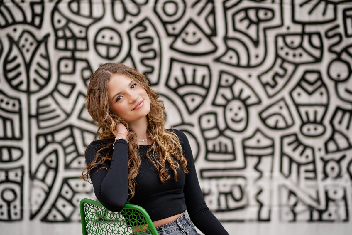 A high school senior girl poses in front of a black and white mural for an urban photo session.