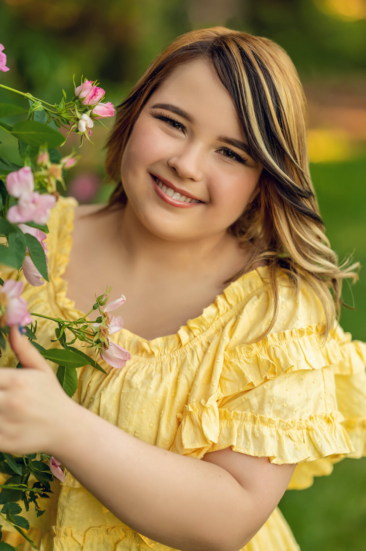 A young woman from Oconomowoc High School leans against a floral trellis wearing a yellow sundress for her senior portraits.