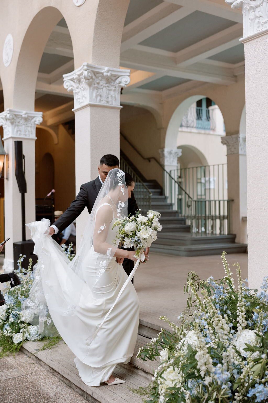 bride and groom during ceremony walking under arches at cafe julia with white and blue flowers surrounding them