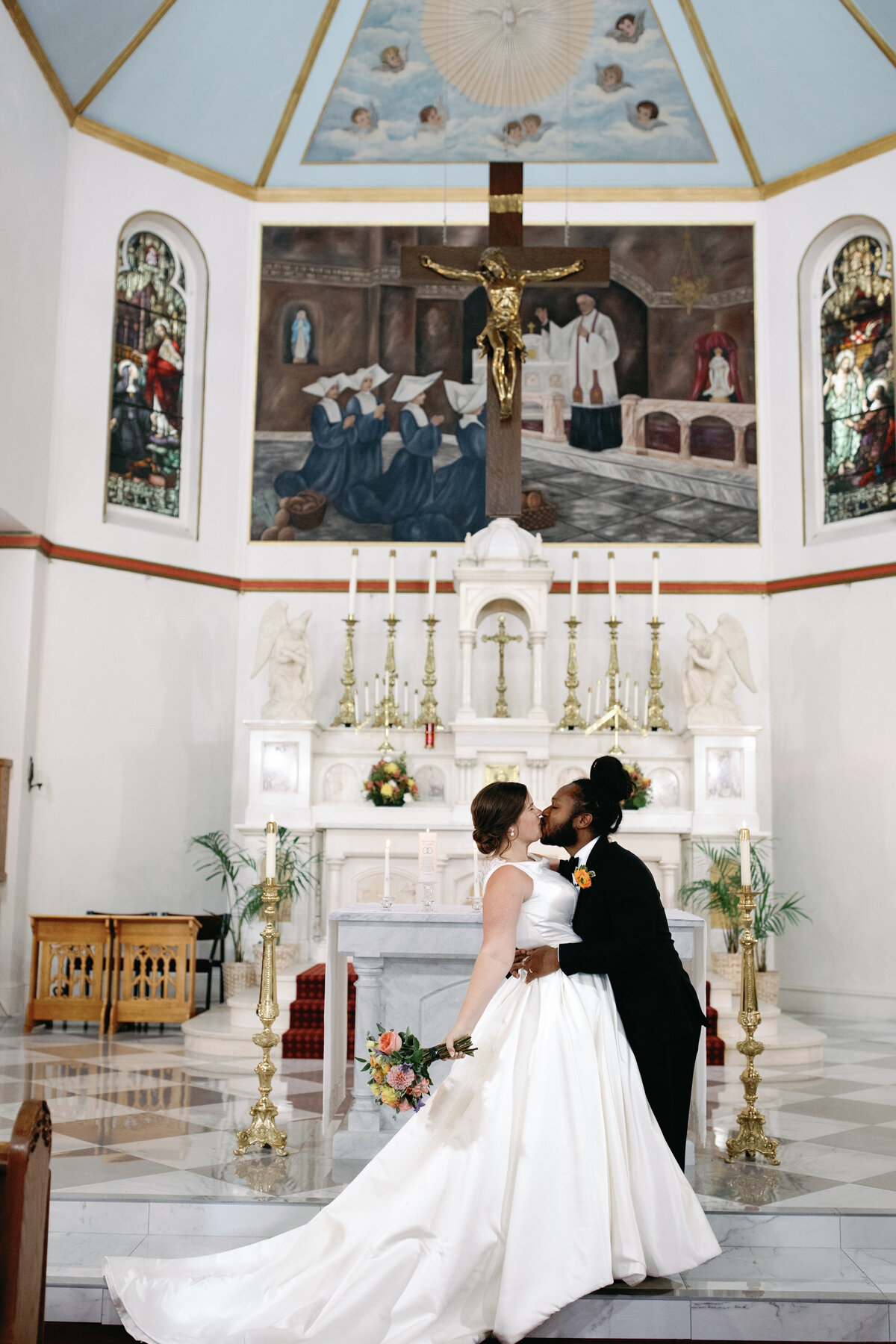 Bride and groom share their first kiss at the altar during Catholic wedding ceremony in Washington DC church.