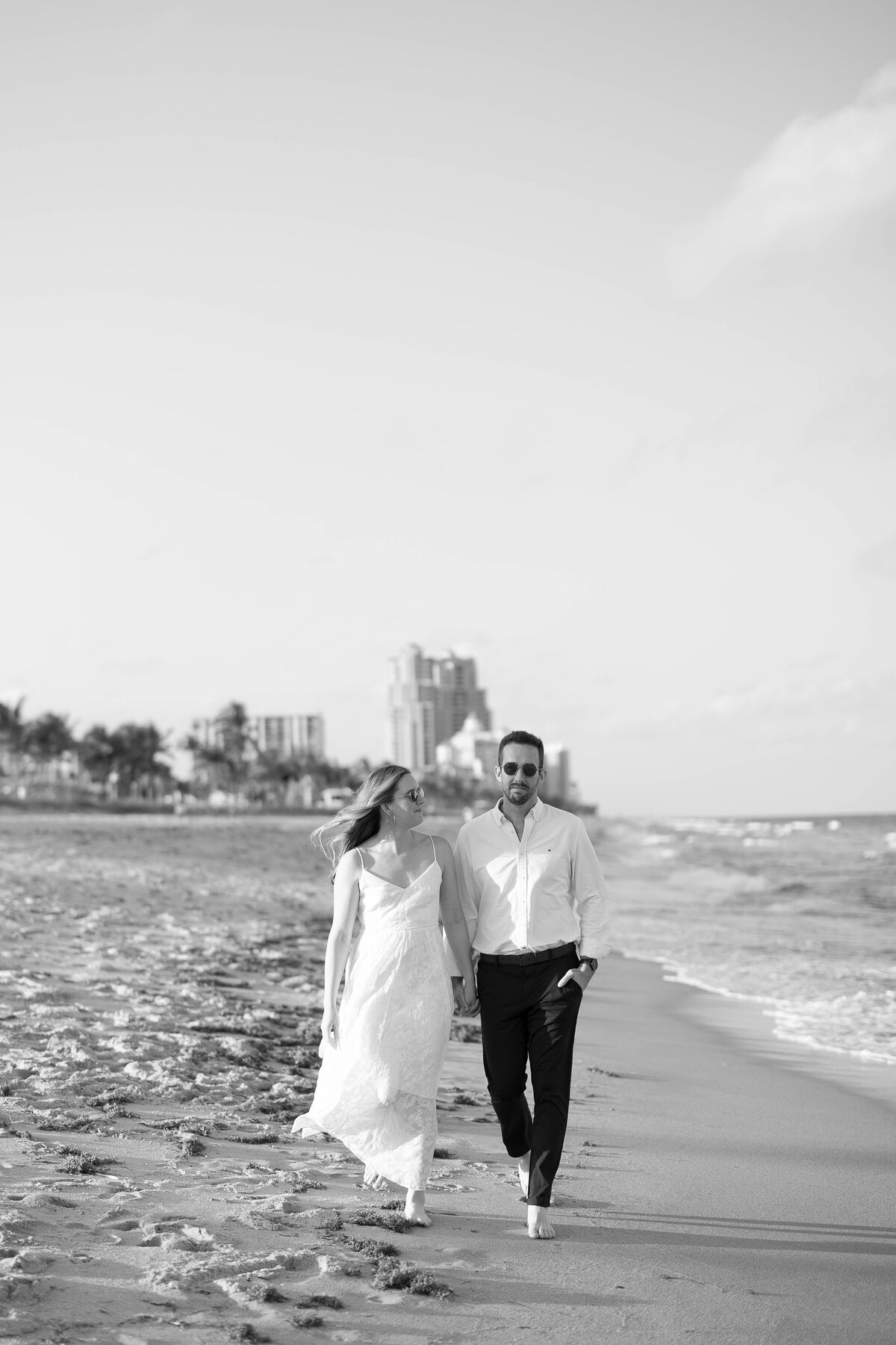 Couple hold hands walking down the shore of the beach