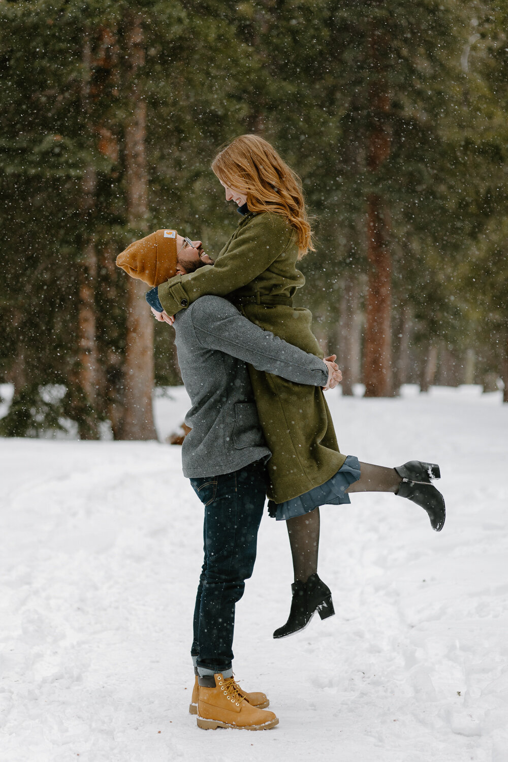 A man lifts his fiancee up in the snow during their Colorado winter engagement session in Denver, Colorado.
