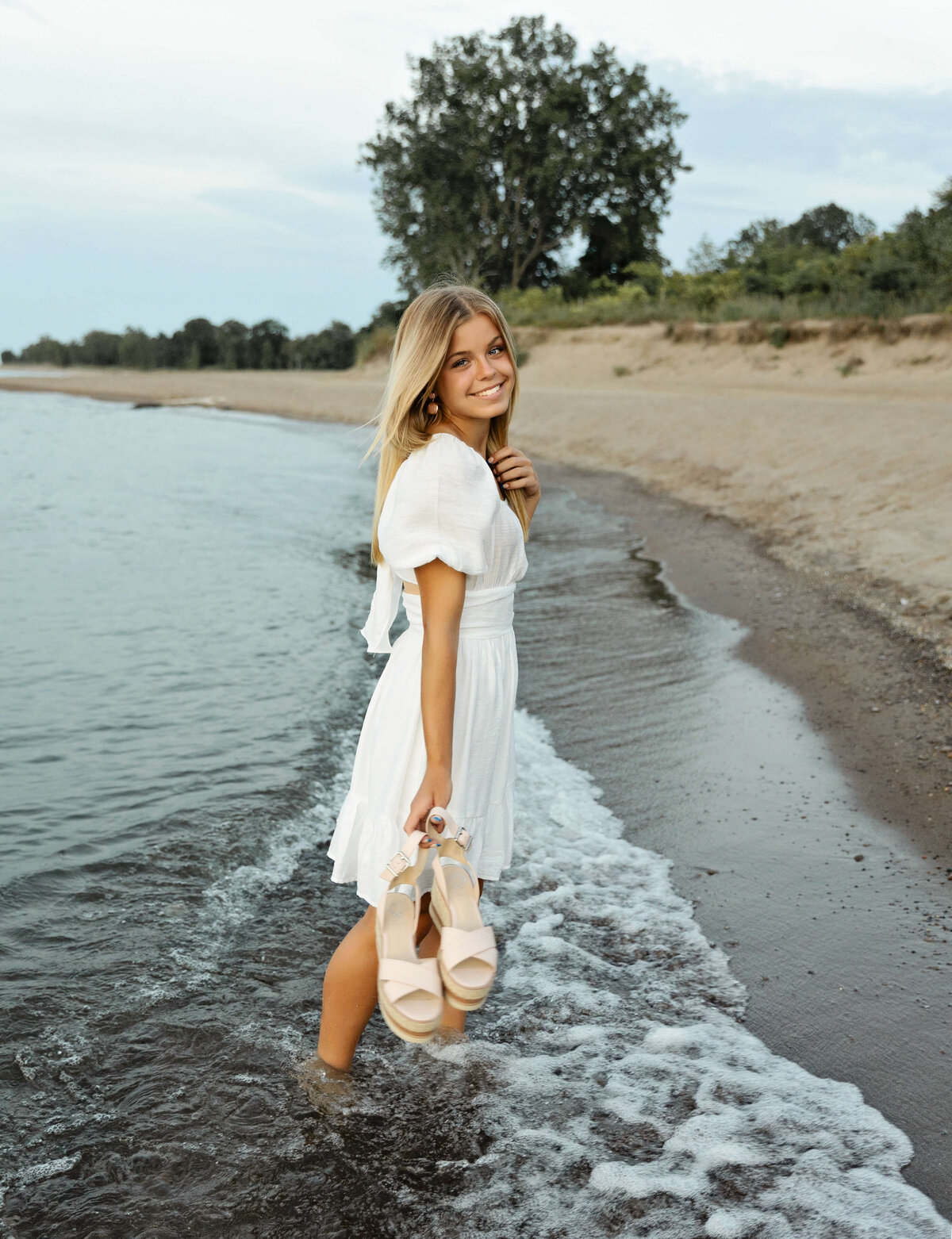 Senior photo of a high school girl standing in the water holding sandals on an Erie Pa beach